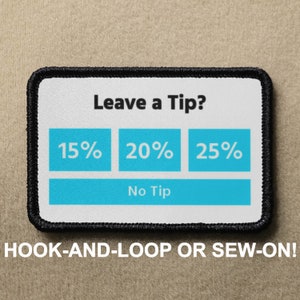 Könnte beinhalten: Ein weißer Patch mit schwarzen Nähten, der einen Trinkgeldrechner mit den Optionen 15 %, 20 %, 25 % und "Kein Trinkgeld" zeigt. Der Text "Trinkgeld geben?" befindet sich oben auf dem Patch. Der Text "HAFTKLETT ODER ANNÄHEN!" befindet sich unter dem Patch.