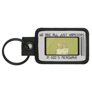 May include: A black and white keychain with a grey and white screen that says "We are all just hamsters in God's microwave". The screen shows a cartoon hamster in a microwave.