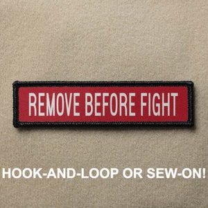 May include: Red and black fabric patch with white text that reads "REMOVE BEFORE FIGHT".