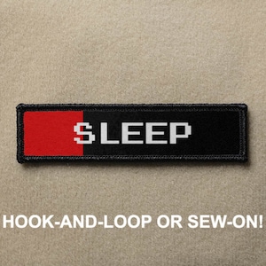 May include: Black and red fabric patch with white text that reads "SLEEP". The patch has a hook-and-loop or sew-on backing.