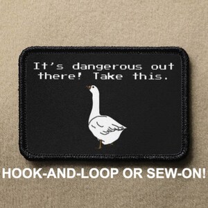 以下が含まれることがあります： 白いガチョウのイラストと「It's dangerous out there! Take this.」というテキストが入った黒い長方形のパッチ。「HOOK-AND-LOOP OR SEW-ON!」とも書かれています。