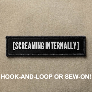May include: Black patch with white text that reads "[SCREAMING INTERNALLY]". The patch is for hook-and-loop or sew-on attachment.