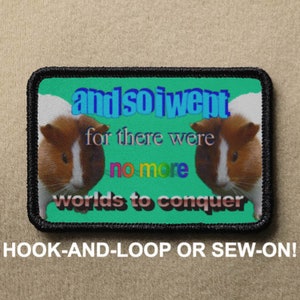May include: Rectangular patch with a black border and a green background. The patch features two guinea pig faces and the text "andsolwent for there were no more worlds to conquer." The text "HOOK-AND-LOOP OR SEW-ON!" is at the bottom.