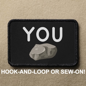 Könnte beinhalten: Schwarzer Patch mit weißem Text, der "YOU" sagt und ein graues Steinbild. Der Patch hat einen schwarzen Rand und sagt "HOOK-AND-LOOP OR SEW-ON!" unter dem Bild.