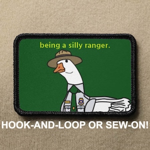 Puede incluir: Parche bordado rectangular con un ganso de dibujos animados vestido con uniforme de guardabosques y sombrero, con el texto "being a silly ranger." El parche tiene un borde negro y está diseñado para ser adherido con velcro o cosido. Fondo verde.