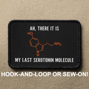 May include: Black patch with white text that reads "AH, THERE IT IS" and a chemical structure with the text "MY LAST SEROTONIN MOLECULE". The patch has black stitching around the edges and the text "HOOK-AND-LOOP OR SEW-ON!" is printed below the patch.