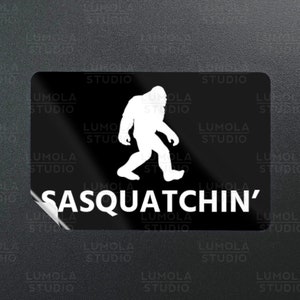 Puede incluir: Pegatina negra y blanca con una silueta de Bigfoot caminando y el texto "Sasquatchin'" en blanco.