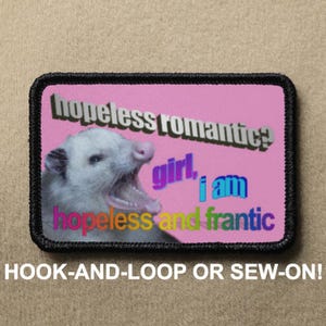 May include: A pink patch featuring a white opossum with rainbow text that reads "hopeless romantic? girl, i am hopeless and frantic".