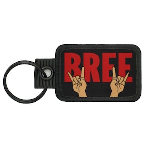 May include: Black key chain with a black and red patch that says "BREE" in red letters with two cartoon hands making the rock and roll hand gesture.