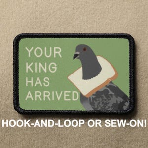 Puede incluir: Un parche bordado verde y negro con un collar de pan blanco alrededor de una paloma gris. El texto en el parche dice "Your King Has Arrived".