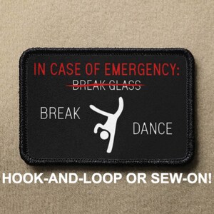 May include: Black and white patch with the text "IN CASE OF EMERGENCY: BREAK GLASS" with a red line through "BREAK GLASS". Below the text is a stick figure breakdancing with the text "BREAK" to the left and "DANCE" to the right. The patch has black stitching around the edges and the text "HOOK-AND-LOOP OR SEW-ON!" is printed below the patch.