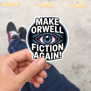 Könnte beinhalten: Ein weißer Aufkleber mit dem Text "MAKE ORWELL FICTION AGAIN!" in einem schwarzen Kreis mit einer Augengrafik. Der Aufkleber wird in einer Hand gehalten, mit einem verschwommenen Hintergrund aus Schuhen und Pflaster.