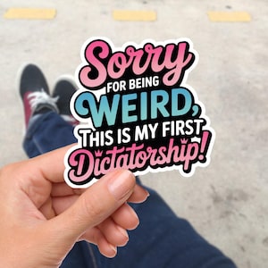 Könnte beinhalten: Eine weiße Keramik-Tasse mit schwarzem Henkel und dem Text "But First, Coffee" in schwarzer, handschriftlicher Schrift. Die Tasse steht auf einer weißen Oberfläche.