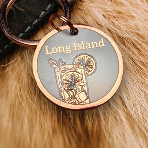 Könnte beinhalten: Ein runder, bronzefarbener Haustieranhänger mit dem Schriftzug "Long Island" in Gold. Der Anhänger zeigt eine detaillierte Illustration eines Cocktails mit Eiswürfeln und einer Zitronenscheibe. Befestigt an einem dunkelgrünen Halsband.