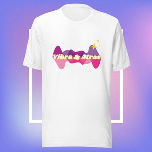 May include: White t-shirt with a pink and purple abstract design and the text "Vibra & Atrae" in yellow.