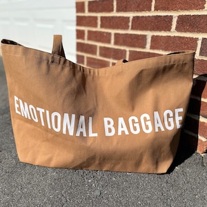 May include: A brown canvas tote bag with white text that reads "EMOTIONAL BAGGAGE".