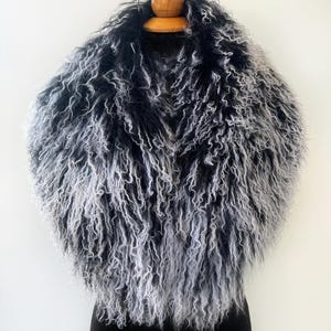 May include: A luxurious faux fur shawl in a blend of black and grey. The shawl is displayed on a wooden hanger, highlighting its voluminous, curly texture. The colour gradient creates a striking visual effect, ideal for adding elegance to any outfit.