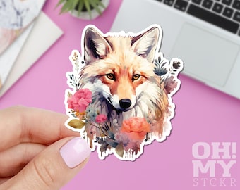 Puede incluir: Una pegatina con una ilustración de acuarela de un zorro con pelaje naranja y blanco, rodeado de flores rosas y azules y vegetación. La pegatina tiene un borde blanco y el texto "OH! MY STCKR" es visible en la esquina inferior derecha.