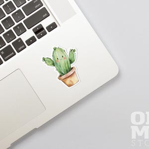 Op de afbeelding: Een aquarel-illustratie van een glimlachende cactus in een bruine pot. De cactus is groen en heeft een paar stekels. De illustratie is op een witte achtergrond.
