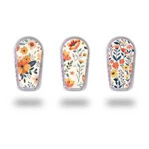 May include: Three white, oval-shaped medical device covers with colorful floral patterns. The patterns feature orange, yellow, red, blue, and green flowers and leaves on a cream background.