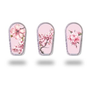Op de afbeelding: Drie roze en witte, met bloemen bedrukte kleefvellen voor een medisch apparaat. De ontwerpen bevatten roze kersenbloesems en een enkele grote roze bloem.