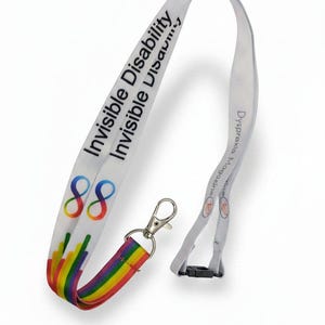 May include: White lanyard with the text "Invisible Disability" and a rainbow design. The lanyard has a silver clasp and a black plastic clip. The design includes the number "88" and the text "Dyspraxia Magazine".