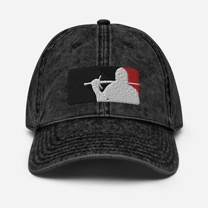 May include: A black denim baseball cap featuring a white embroidered image of a person holding a sword. The image is set against a black and red background.