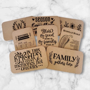 May include: Set of eight brown wooden kitchen signs with black text. The signs feature various kitchen-themed sayings, including "In this kitchen we count memories not calories", "Family gathers here", "Bless the food before us the family beside us", and "Season everything".