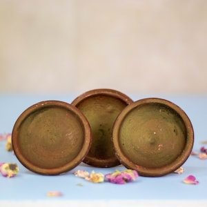 Puede incluir: Tres platos de terracota, cada uno con un tono de marrón ligeramente diferente, están dispuestos sobre una superficie azul claro. Los platos están vacíos y tienen una superficie lisa ligeramente texturizada.