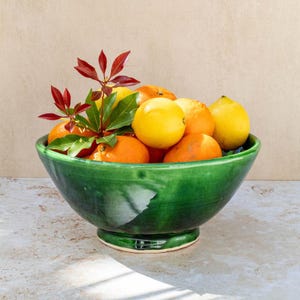 May include: A green ceramic bowl filled with a variety of citrus fruits, including oranges and lemons. The bowl has a decorative glaze and a wide rim.