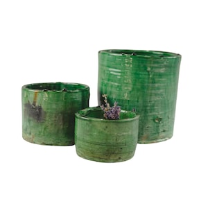 May include: Three green ceramic pots of varying sizes. The largest pot is taller and wider than the other two. The smallest pot has a sprig of lavender inside.