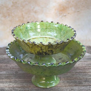 Può includere: Piatto da portata in ceramica fatto a mano a due livelli. Le ciotole smaltate verdi hanno un bordo smerlato con accenti scuri. La base è in stile piedistallo e le ciotole sono impilate. Il piatto è su una superficie di legno.