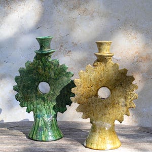 Puede incluir: Dos esculturas de cerámica, una verde y otra amarilla. Cada una tiene un diseño único con una abertura circular y forma de sombrero de copa. Se exhiben sobre una superficie de madera. Son decorativas.