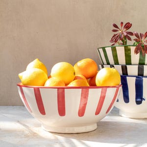 May include: A white ceramic bowl with red stripes, filled with lemons and oranges. The bowl is sitting on a light grey surface.