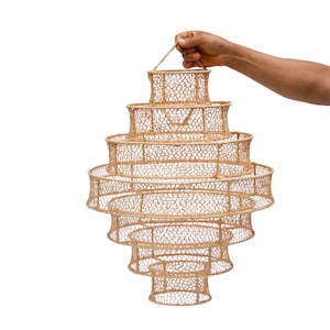 May include: A woven pendant light fixture made from natural materials. The light fixture is made of multiple layers of woven material, creating a tiered effect. The light fixture is suspended from a single point and has a natural, earthy colour.