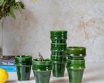 May include: A set of six green ceramic cups with a textured finish. The cups are stacked in a pyramid shape, with the largest cup at the bottom and the smallest cup at the top.