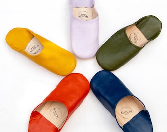 May include: Six pairs of leather slippers in different colors, including yellow, orange, red, blue, green, and purple. Each slipper has the text "Maison Premiere" printed on the inside.