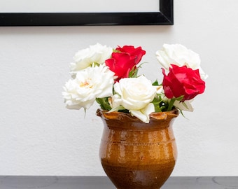 Puede incluir: Un ramo de rosas blancas y rojas arreglado en un jarrón de cerámica marrón con un diseño decorativo.