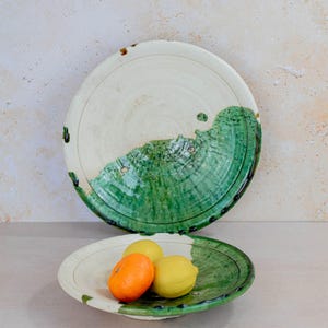 以下が含まれることがあります： 2つのセラミック製サービング皿。大きな皿は白で、緑の波模様があります。小さな皿には、みかんとレモンが2つ入っています。手作りで素朴な雰囲気の皿です。