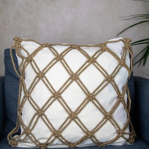 Op de afbeelding: Een wit kussen met een bruin touwnetontwerp. Het kussen ligt op een blauwe bank.