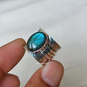 May include: A silver ring featuring a large oval blue labradorite gemstone set in a wide band. The band is textured with a floral design.