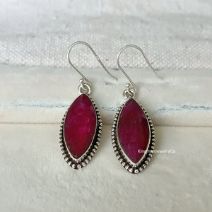 Puede incluir: Un par de pendientes de plata con una piedra preciosa roja en forma de marquesa. Los pendientes tienen un borde de cuentas alrededor de la piedra preciosa.