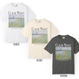 May include: Three short-sleeved t-shirts in white, ivory, and pepper gray. Each shirt features a rectangular print of a Claude Monet painting with the artist's name above the artwork. The shirts are made of a soft material.