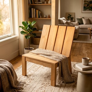 May include: A light-toned wooden chair featuring a backrest composed of four vertical slats and a flat seat. A textured, beige waffle-knit throw blanket is draped over the seat of the chair, extending down toward the floor in soft folds.