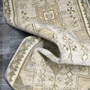 May include: A vintage rug with a beige background and a green border. The rug has a traditional floral pattern and a central medallion.