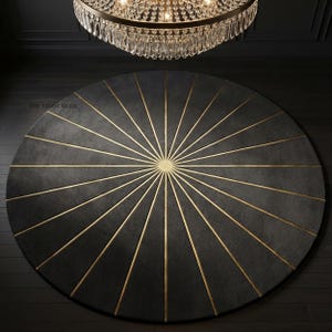 May include: A circular dark gray rug featuring a central gold sunburst pattern with radiating lines extending to the edges. The text THE LIGHT RUGS is printed in small black letters on the upper left side of the rug, which sits on a dark floor.