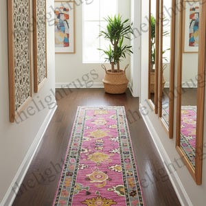 May include: A long, rectangular pink rug with a detailed floral pattern in yellow, green, and blue. The rug is placed on a dark wood floor in a hallway, with mirrors and artwork on the walls. The rug measures approximately 8 feet long.