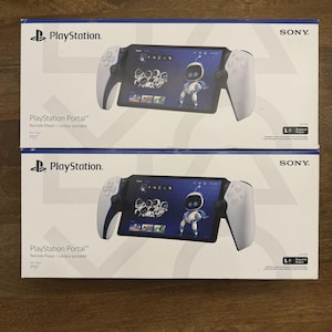 May include: Two white and blue PlayStation Portal boxes are stacked on a wooden surface. Each box features the PlayStation logo, the product name, and a graphic of the device displaying a character. The Sony logo is visible on the top right corner.