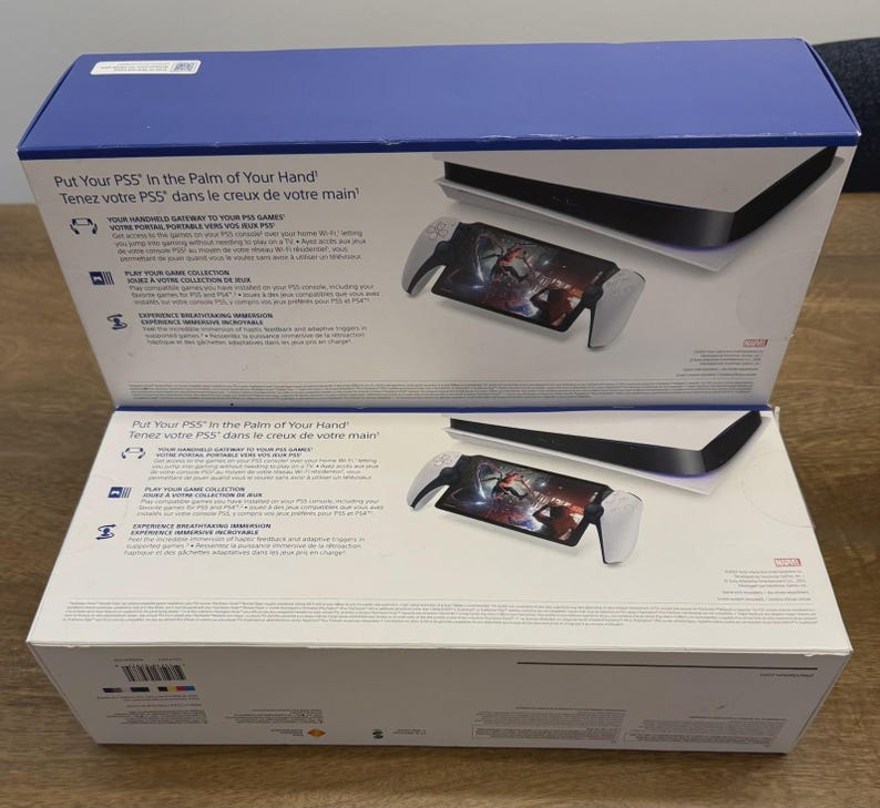 May include: Two white and blue PS5 boxes are open, revealing a console and a handheld device with a screen displaying a game. The boxes have text in English and French. The handheld device has white handles and a black screen.