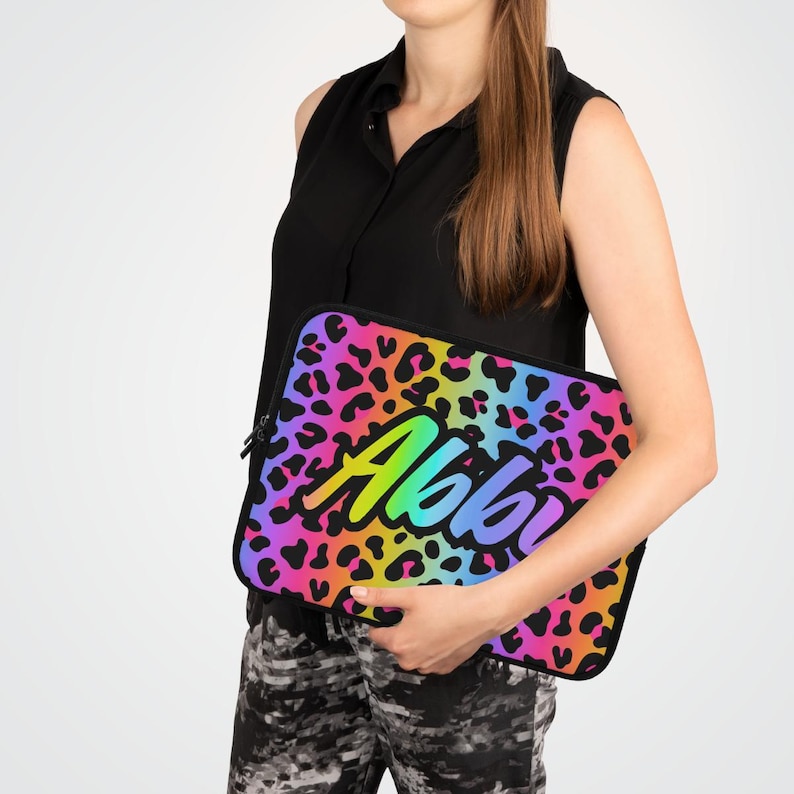 May include: A laptop sleeve with a rainbow leopard print design and the name "Abbi" in a rainbow font.